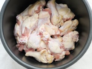下ごしらえした鶏手羽元を、電気圧力鍋の内釜に並べ入れた様子（甘辛煮の調理工程）