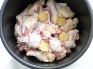 電気圧力鍋に並べた鶏手羽元の上に、生姜の薄切りをのせたところ（臭み消し用）
