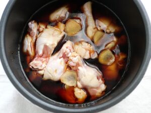 電気圧力鍋に鶏手羽元・生姜・煮汁を入れ終えた様子（甘辛煮の加圧前の状態）