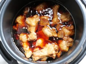 電気圧力鍋のふたを開け、鶏手羽元の甘辛煮を煮詰めて仕上げている様子