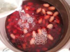 さし水をして鍋の温度を下げ、金時豆のアクをさらに抜いている様子