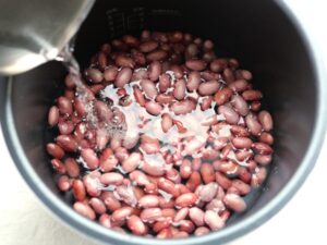 電気圧力鍋の内釜で、煮汁に浸りきっていない金時豆に水を少量注ぎ足しているところ