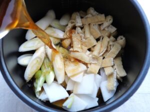 内鍋の大根、長ねぎ、油揚げに、だし汁の1/3と調味料を混ぜて注いでいる様子