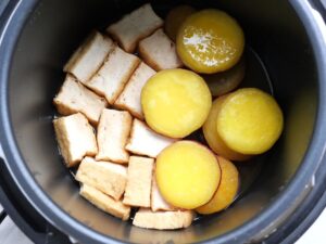圧力調理後の電気圧力鍋の中の様子。煮汁がしみ込んだ厚揚げと、火が通って黄金色になったさつまいもが見える