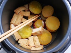 菜箸でさつまいもを裏返し、厚揚げの白い部分を煮汁に浸けた状態。煮込み直前の様子