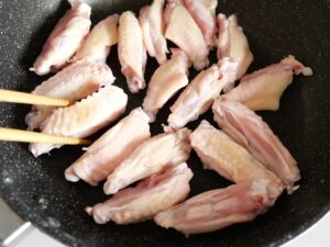 フライパンで焼いている鶏手羽中。電気圧力鍋で甘辛煮にする下ごしらえ工程