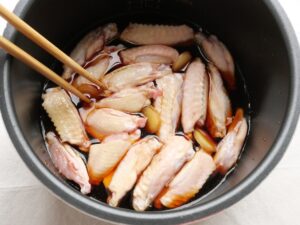 鶏手羽中を菜箸で動かし、煮汁に浸ける工程