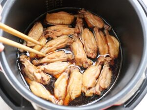 菜箸で鶏手羽元を裏返し、煮汁に浸けている様子