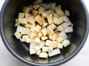電気圧力鍋の内釜に玉ねぎとさつまいもを重ね、顆粒コンソメをふりかけた下味付けの工程