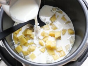 電気圧力鍋の内釜に牛乳を注ぎ入れる工程。煮込み前の下準備