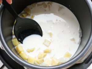 白いミルクスープの中でスプーンでさつまいもを潰す工程。なめらかな口当たりに仕上げる