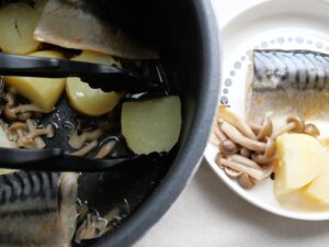 トングで塩さばと野菜を電気圧力鍋から取り出して、皿に盛り付けているところ