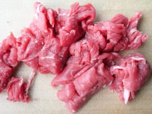 牛肉の切り落としをまな板の上で一口大に切ったところ
