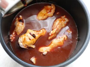 煮汁を注ぎ終えた電気圧力鍋の中。鶏手羽元の一部が煮汁から出ている様子