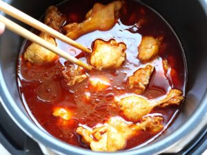 鶏手羽元を菜箸で返しながら煮汁に浸しているところ（煮込み前）