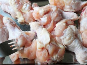 鶏手羽元にフォークで穴を開けて下ごしらえしている様子（電気圧力鍋で調理する前）