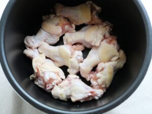 電気圧力鍋の内釜に下ごしらえした鶏手羽元を並べた状態
