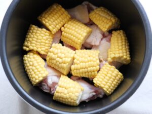 鶏手羽元の上に、縦半分のとうもろこしを芯を下にして並べ入れた状態