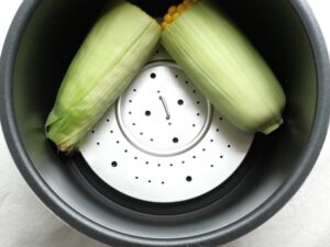 蒸し板の上に、半分に切った皮付きのとうもろこしを並べた状態