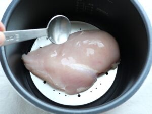 蒸す前の鶏むね肉に酒をかけている様子。臭み消しとしっとり仕上げるための工夫