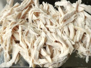 蒸し上がった鶏むね肉を手で裂き終わった状態。トレイの上に並んでいる