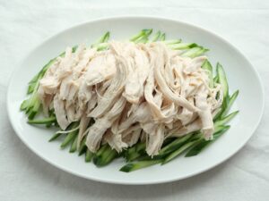 千切りきゅうりの上に裂いた鶏むね肉を盛り付けたところ。中華だれをかける直前