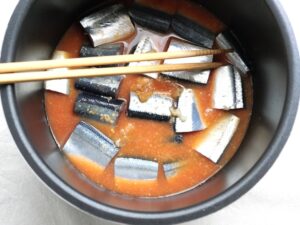 電気圧力鍋の煮汁の中に、さんまの切り身が浸るように菜箸で沈めているところ。圧力調理直前の状態