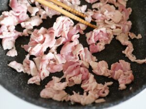 フライパンで豚肉を炒め、菜箸でほぐしている様子