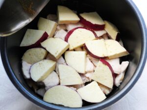 鶏むね肉の上にさつまいもを重ね、水と顆粒コンソメを混ぜた煮汁を注いでいる様子