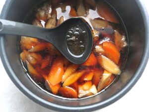 炒め煮の煮汁に浮いたアクをお玉ですくっている様子