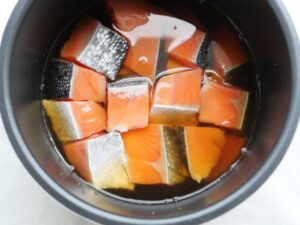 電気圧力鍋の内釜で塩鮭が煮汁に浸かった様子（圧力調理直前の様子）