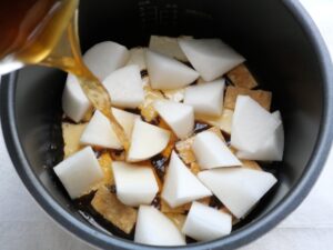 電気圧力鍋の内釜に、だし汁・醤油・砂糖・みりんを混ぜた煮汁を注いでいるところ