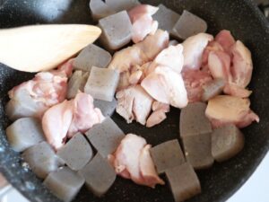 鶏もも肉と角切りこんにゃくをフライパンで炒めている様子。具材に油がまわり始めている