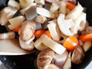 筑前煮の具材（鶏肉・こんにゃく・人参・しいたけ・ごぼう・れんこん）をフライパンで炒めている様子
