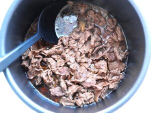 電気圧力鍋の具材をスプーンでかき混ぜ、煮汁に浸している様子