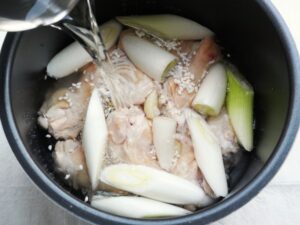 鶏手羽元、長ねぎの上から煮汁を注いでいるところ