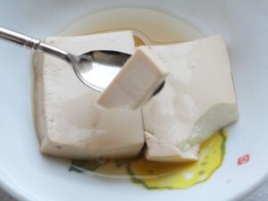 スプーンですくった木綿豆腐。表面が薄茶色に色付き、味がしみている様子。