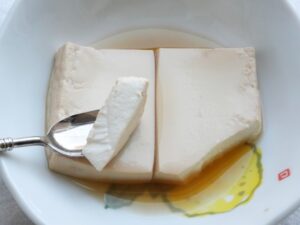 スプーンですくった木綿豆腐。表面が茶色に色付き、味がしみている様子。