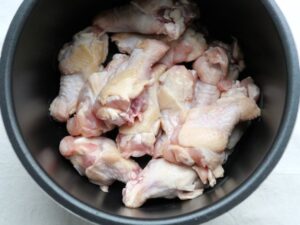 下ごしらえした鶏手羽元を、電気圧力鍋の内釜に並べ入れた様子