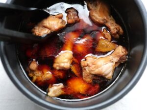 内釜の鶏手羽元をトングで返して甘辛の煮汁に浸している工程