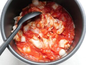 内釜の具材をシリコンスプーンで混ぜ合わせ、カットトマトを全体になじませた様子