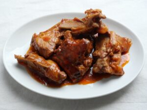白い器に盛り付けた、スペアリブのBBQ煮込み。赤茶色で照りのある仕上がり