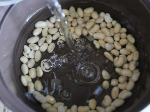 大豆を入れた鍋に新しい水を注いでいる様子